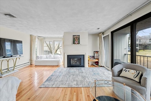 living area featuring a healthy amount of sunlight, a glass covered fireplace, hardwood / wood-style floors, and visible vents