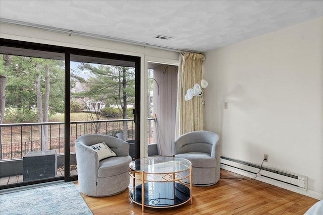 sitting room featuring a baseboard heating unit, wood finished floors, and visible vents