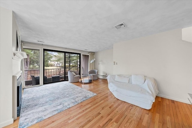 living area featuring visible vents, wood finished floors, a fireplace, baseboards, and a baseboard heating unit