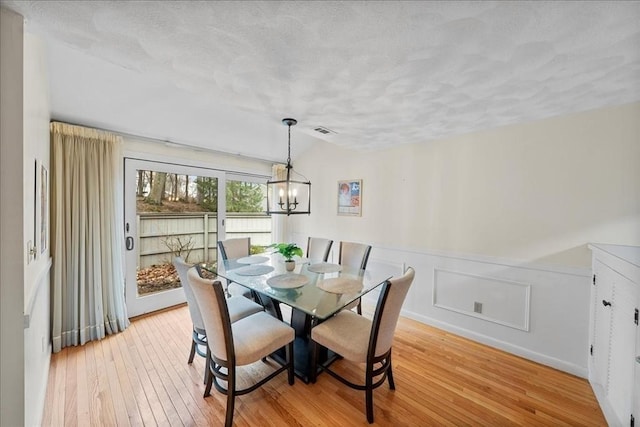 dining area with a notable chandelier, light wood-style floors, a wainscoted wall, lofted ceiling, and visible vents