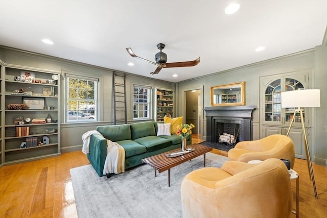 living area with a fireplace with flush hearth, built in shelves, hardwood / wood-style floors, crown molding, and ceiling fan