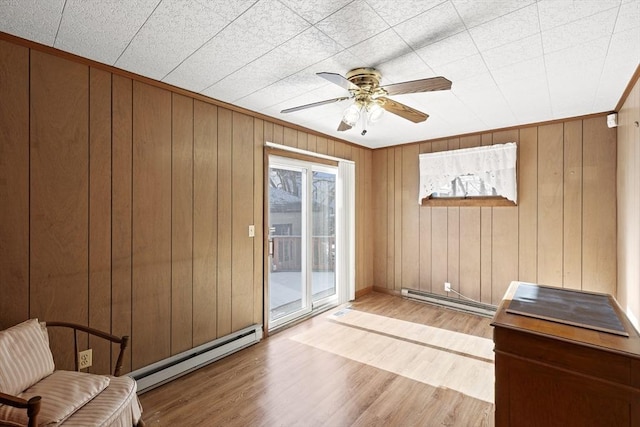 doorway featuring ceiling fan, light hardwood / wood-style floors, wooden walls, and a baseboard heating unit