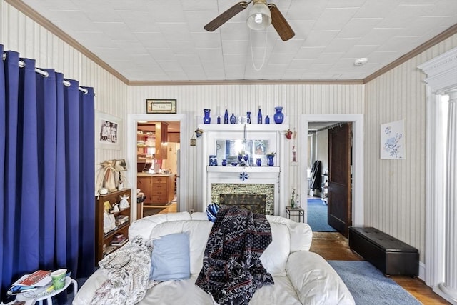 living room featuring ceiling fan, crown molding, wood-type flooring, and a fireplace