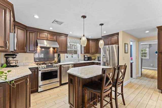 kitchen featuring visible vents, appliances with stainless steel finishes, a center island, under cabinet range hood, and pendant lighting