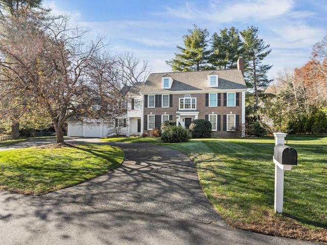 colonial-style house with a garage, aphalt driveway, a chimney, and a front yard