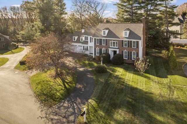 view of front of home featuring driveway, a chimney, and a front yard