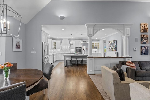 dining space featuring light wood-type flooring, vaulted ceiling, a notable chandelier, and ornate columns