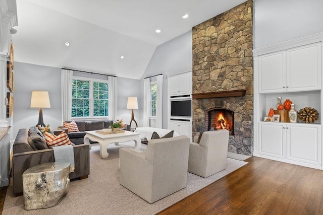 living room featuring hardwood / wood-style flooring, vaulted ceiling, and a stone fireplace