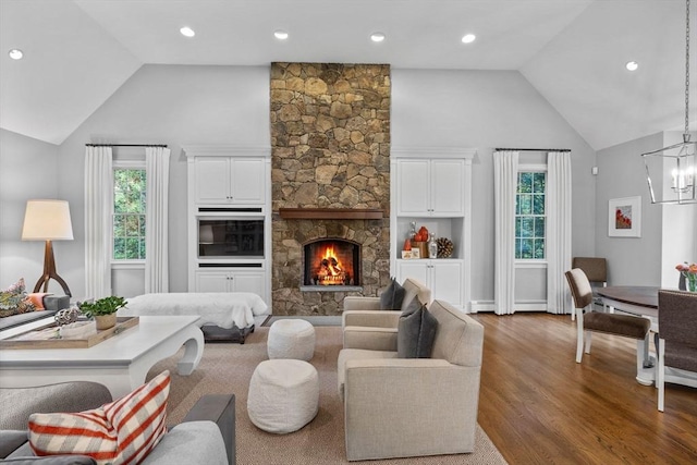 living room with hardwood / wood-style flooring, a wealth of natural light, built in shelves, and a stone fireplace