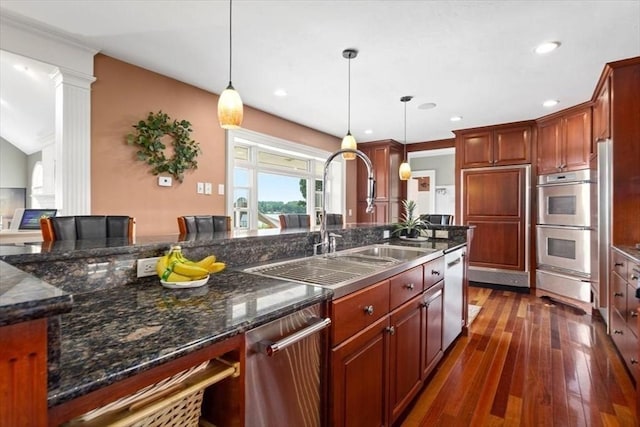 kitchen with sink, dark wood-type flooring, dark stone countertops, stainless steel appliances, and decorative light fixtures