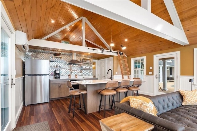 kitchen with a breakfast bar, wooden ceiling, stainless steel refrigerator, wall chimney range hood, and backsplash