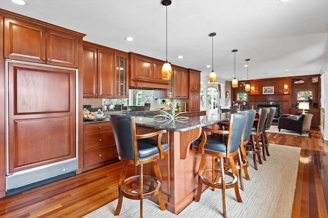 kitchen featuring decorative light fixtures, a breakfast bar area, dark stone countertops, dark hardwood / wood-style flooring, and a kitchen island with sink