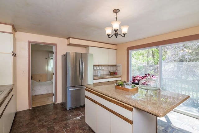 kitchen with backsplash, stone finish flooring, hanging light fixtures, white cabinets, and freestanding refrigerator