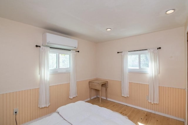 bedroom with wainscoting, a wall unit AC, and multiple windows