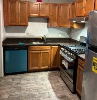 kitchen featuring stainless steel appliances, dark countertops, a sink, and under cabinet range hood