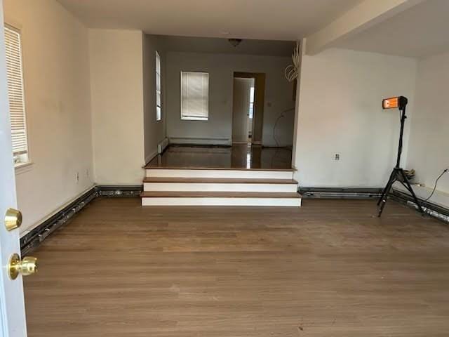 spare room featuring a baseboard heating unit, stairs, beamed ceiling, and wood finished floors