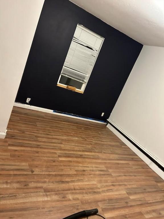 empty room with a baseboard heating unit, wood finished floors, and baseboards