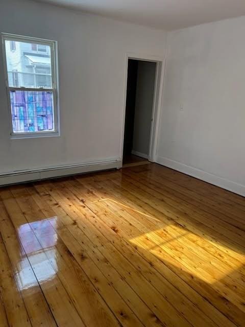 unfurnished room with a baseboard heating unit, light wood finished floors, and baseboards