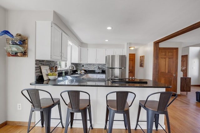 kitchen featuring a peninsula, freestanding refrigerator, white cabinetry, backsplash, and black stovetop