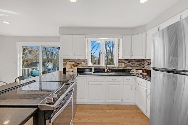 kitchen featuring light wood-type flooring, electric stove, a sink, white cabinetry, and freestanding refrigerator