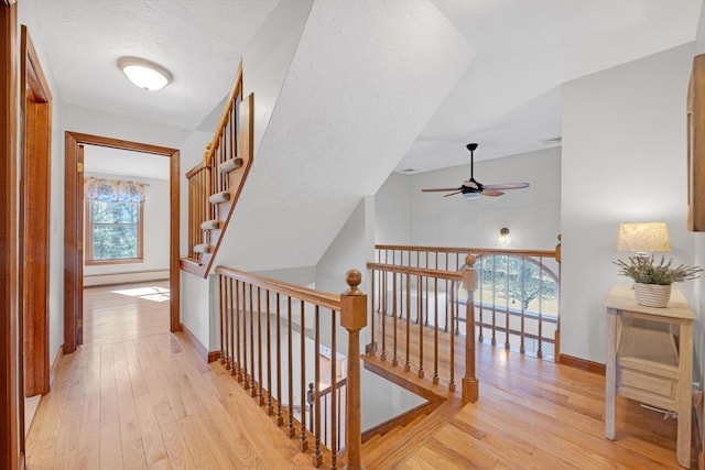 hall featuring an upstairs landing, light wood-type flooring, and baseboards