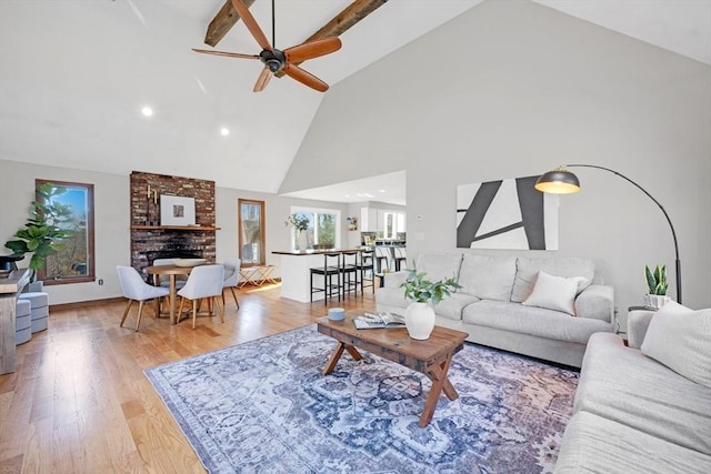 living area featuring high vaulted ceiling, a fireplace, light wood finished floors, and ceiling fan