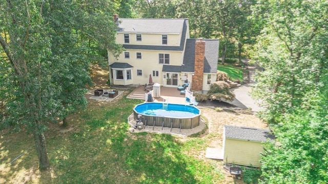 back of house with an outdoor pool, a wooden deck, a lawn, and a chimney