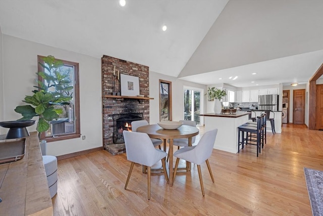 dining room featuring baseboards, recessed lighting, a fireplace, light wood-style floors, and high vaulted ceiling