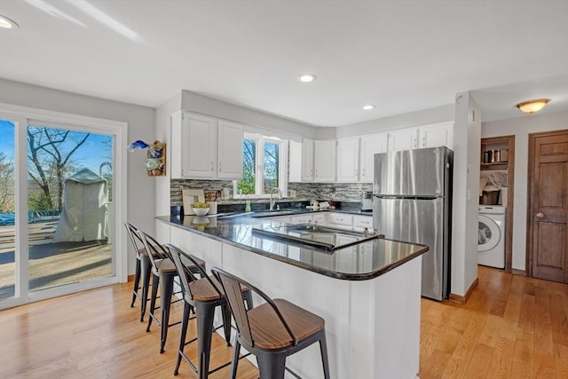 kitchen with a sink, dark countertops, freestanding refrigerator, cooktop, and washer / dryer