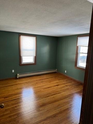 unfurnished room with wood-type flooring, a textured ceiling, and a baseboard heating unit