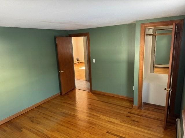 unfurnished bedroom with a closet, baseboard heating, and light wood-type flooring