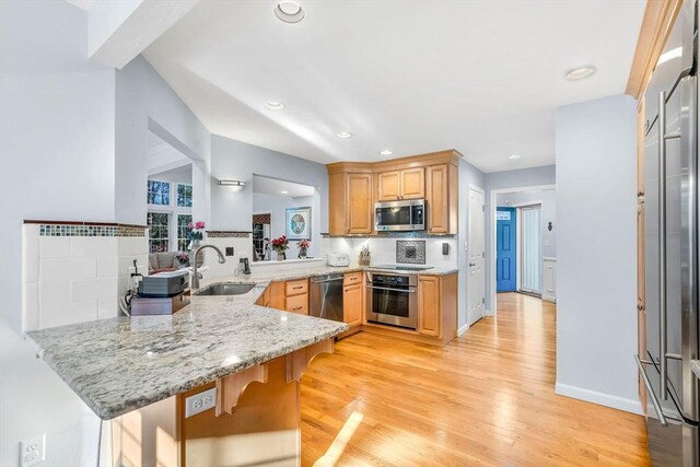 kitchen with kitchen peninsula, a breakfast bar area, decorative backsplash, light stone countertops, and appliances with stainless steel finishes