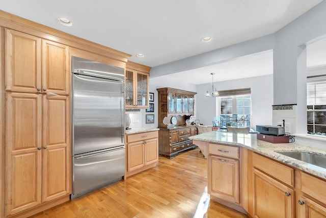 kitchen with light stone counters, light hardwood / wood-style flooring, hanging light fixtures, a notable chandelier, and built in refrigerator