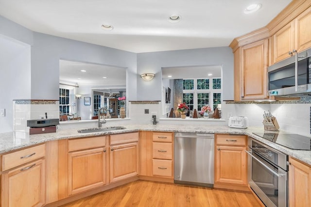 kitchen with stainless steel appliances, light wood-type flooring, kitchen peninsula, light brown cabinets, and sink