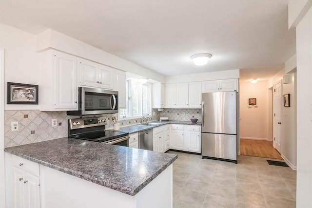 kitchen with appliances with stainless steel finishes, a peninsula, and white cabinetry