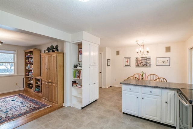 kitchen with a notable chandelier, pendant lighting, stainless steel range with electric cooktop, white cabinets, and baseboards