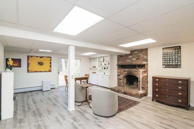 living area with a drop ceiling, a baseboard heating unit, a brick fireplace, and wood finished floors