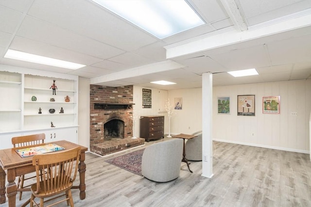 living area with light wood finished floors, built in shelves, baseboards, a drop ceiling, and a fireplace