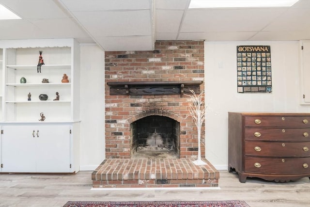 unfurnished living room featuring light wood finished floors, a fireplace, a paneled ceiling, and baseboards