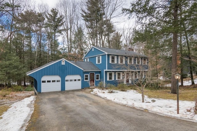 view of front of property featuring aphalt driveway, an attached garage, covered porch, and a chimney