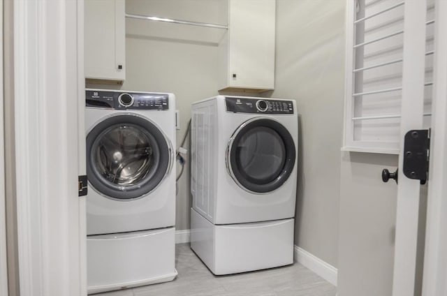 clothes washing area with washer and clothes dryer, cabinets, and light wood-type flooring