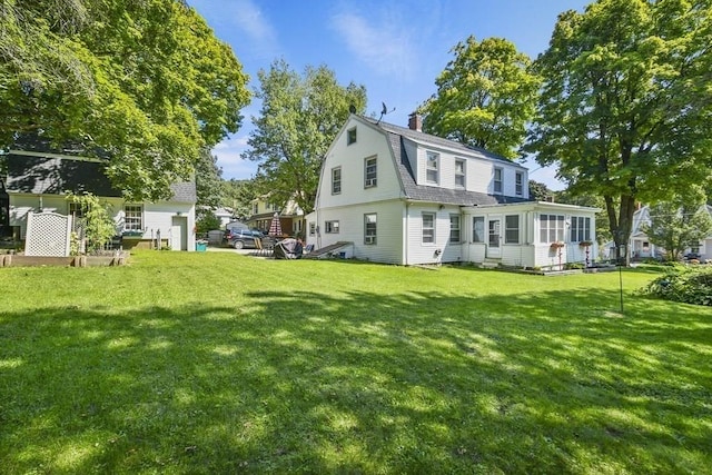 rear view of property with a shingled roof, a chimney, a lawn, and a gambrel roof