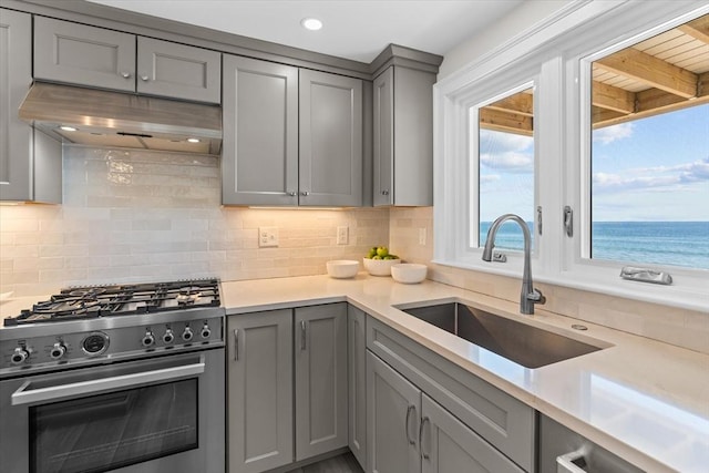 kitchen with gray cabinetry, high end stainless steel range oven, decorative backsplash, and a sink