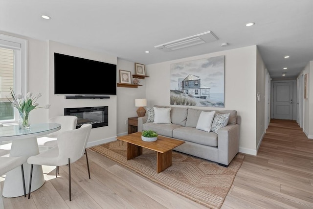 living room with a glass covered fireplace, light wood-style floors, recessed lighting, and baseboards