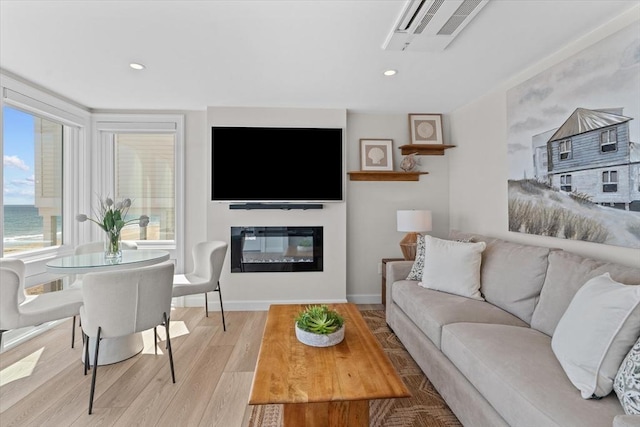 living room featuring recessed lighting, light wood-style floors, a glass covered fireplace, visible vents, and baseboards