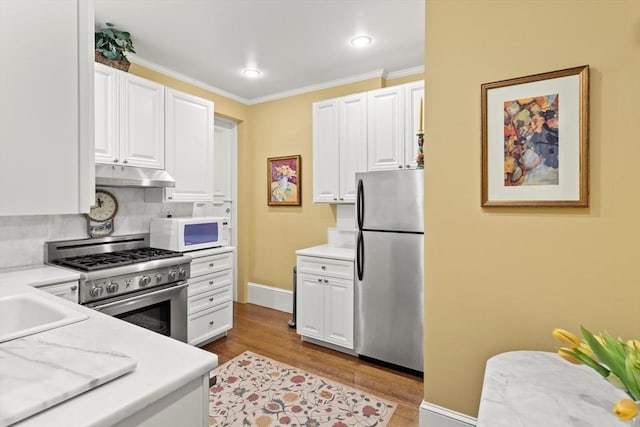kitchen with appliances with stainless steel finishes, under cabinet range hood, light countertops, and crown molding