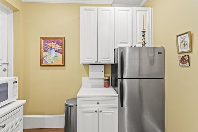 kitchen featuring freestanding refrigerator, white microwave, white cabinets, light countertops, and baseboards