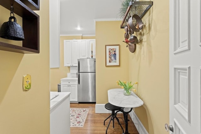 corridor with light wood-style floors, ornamental molding, and baseboards