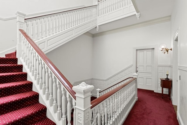 stairway featuring carpet floors, wainscoting, ornamental molding, and a decorative wall