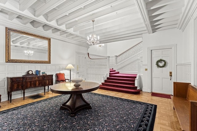 entrance foyer featuring a decorative wall, a chandelier, stairs, beamed ceiling, and a wainscoted wall